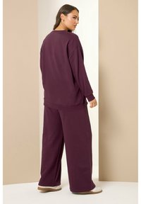 Stort, djupt burgundy sweatshirt och vida byxor i ett mjukt, texturerat tyg. Enkel design, ribbade ärmslut och avslappnad passform.