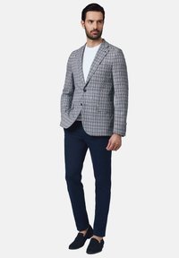 Jasnoszary marynarka w kratę z czarnymi i niebieskimi akcentami, biały t-shirt, granatowe spodnie i czarne buty wsuwane. Gładki materiał, dopasowany krój.