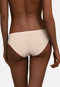 Beżowy bezszwowy figowy bikini o gładkiej teksturze i niskim stanie, wyposażony w miękką, elastyczną gumkę i minimalistyczny fason zapewniający skromne zakrycie.