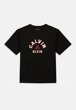 T-shirt noir à manches courtes avec col rond, affichant "CALVIN" en arc de cercle et "KLEIN" en lettres majuscules, centrés en texte rose clair.