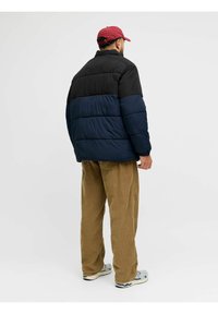 Gepolsterte Jacke mit einem schwarzen oberen Abschnitt und einem marineblauen unteren Abschnitt. Verfügt über einen hohen Kragen, elastische Bündchen und ein glattes Finish. Wird mit beigen Cordhosen getragen.