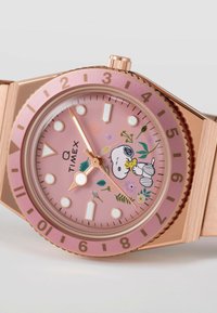 Timex ur med lyserød urskive, rosaguld kabine og blomsterdesign med Snoopy. Uret har tykke time- og minutvisere, lysende markører og en bezel.