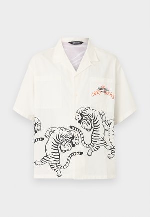 Chemise blanche à manches courtes avec des motifs de tigre noirs le long du bas et le texte "The Crazy Numbers Just Cavalli Milano" sur la zone de la poche poitrine.