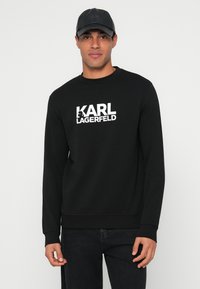 Čierna mikina s okrúhlym výstrihom a dlhými rukávmi. V strede biela potlač "KARL LAGERFELD". Mäkká, textúrovaná látka.