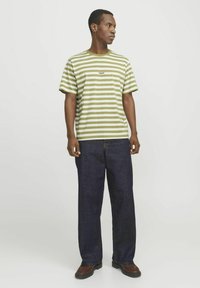 Oliven grøn og hvid stribet t-shirt med rund hals, parret med mørkeblå vide jeans og brune lædersko. Simpelt design.
