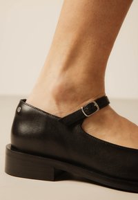 Αστραγάλός με μαύρο δερμάτινο παπούτσι Mary Jane με μικρό τακούνι και ρυθμιζόμενο λουράκι με πόρπη.