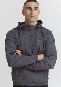 Gray pullover jacket made of lightweight material, featuring a half-zip front, adjustable hood, elastic cuffs, and a small logo patch.