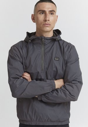 Gray pullover jacket made of lightweight material, featuring a half-zip front, adjustable hood, elastic cuffs, and a small logo patch.