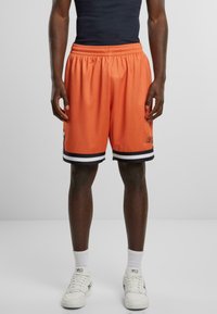 Orange mesh basketballshorts med sort og hvid stribet kant, elastisk talje og lille logo på den nederste side.