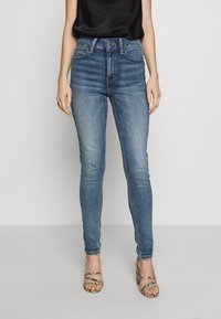 Riflové džíny s vysokým pasem, slim fit, s jemným vyblednutím, pěti kapsami a zipem. V páru s páskovými lodičkami z hadí kůže.