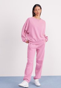 Roze, oversized sweatshirt met geribde manchetten en onderrand, gecombineerd met bijpassende joggers. Beide gemaakt van zachte stof en voorzien van zijzakken.