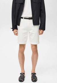 Shorts in denim bianco con orli arrotolati, abbinati a una giacca nera e sandali intrecciati neri, caratterizzati da un design semplice e linee pulite.