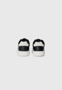 Zwart-witte leren sneakers met een textured achterpaneel, rubberen zool en subtiele branding op de hak. Rond toel ontwerp.