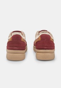 Červené zúžené tenisky z semišu s béžovými doplnkami, textúrovaným golierom a gumovou podrážkou. Obsahujú polstrovaný interiér pre pohodlie a štýl.