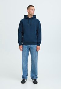Mønstret hettegenser i marineblå med frontlomme, snor til hetten og svart logo. Sammen med lyseblå jeans og svarte joggesko.