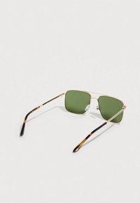 Gold-framed square sunglasses with green lenses and tortoiseshell-patterned temple tips resting on a white surface.