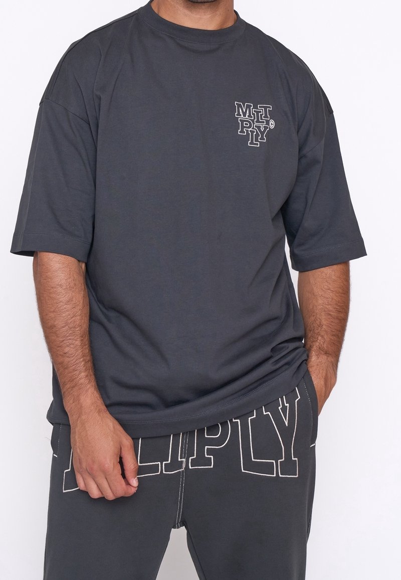 T-shirt à manches courtes gris foncé en coton. Présente un petit logo sur le côté gauche de la poitrine et une coupe décontractée avec des épaules tombantes.