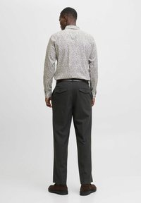Camicia a maniche lunghe con motivo floreale bianca e vari colori. Pantaloni grigi scuri a gamba dritta con tasche posteriori. Scarpe in suede marroni.