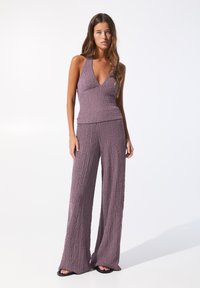 Lilla to-delt outfit bestående af en ærmeløs halterneck top med en tekstureret overflade og brede bukser. Stoffet ser blødt og krøllet ud.