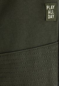 Πράσινα αθλητικά σορτς με υφασμένη, ριμπ υφή μέση και ορθογώνια ετικέτα που γράφει "ΠΑΙΞΕ ΟΛΗ ΜΕΡΑ" σε λευκό κείμενο.