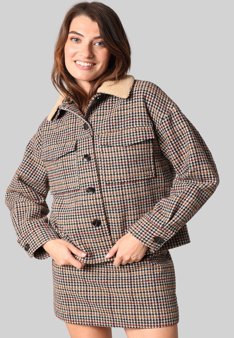 Havanna-patroon jas met een beige kraag, voorzien van zwarte knopen en twee voorkruiden. De stof heeft een gestructureerde, geweven uitstraling.