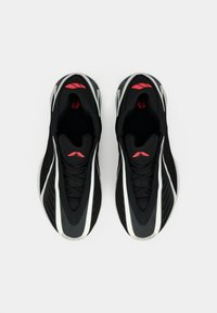 Μαύρα αθλητικά παπούτσια με υφή στην επιφάνεια, λευκές ρίγες και κόκκινες λεπτομέρειες. Διαθέτουν σχέδιο με κορδόνια και άνετο εσωτερικό.