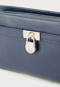 Modra usnjena denarnica z teksturirano površino, srebrnkasto kovinsko opremo, zadrgo in obeskom z logotipom z začetnicama "MK".