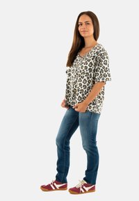 Top de manga corta y escote en V en tejido ligero con un patrón de leopardo; combinado con jeans azules y zapatillas rojas con acentos en blanco.