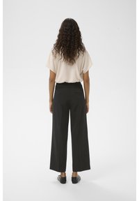 Beige kortärmad topp, svarta vida byxor och svarta platta skor. Slät tygtextur och enkel design, sedd bakifrån.