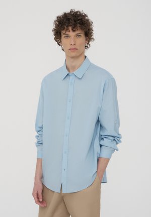 Camicia button-up azzurro chiaro con colletto a punta, maniche lunghe e polsini arrotolati, realizzata in un tessuto liscio con una sottile texture.