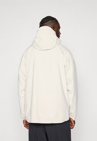 Lightweight, cream-colored jacket with a hood. Features elastic cuffs and a relaxed fit, made from smooth, textured material.