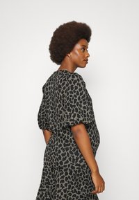 Vestido de estampa de leopardo em verde e preto, com mangas bufantes e saia em camadas. Tecido suave com um corte descontraído, adequado para vestuário de maternidade.