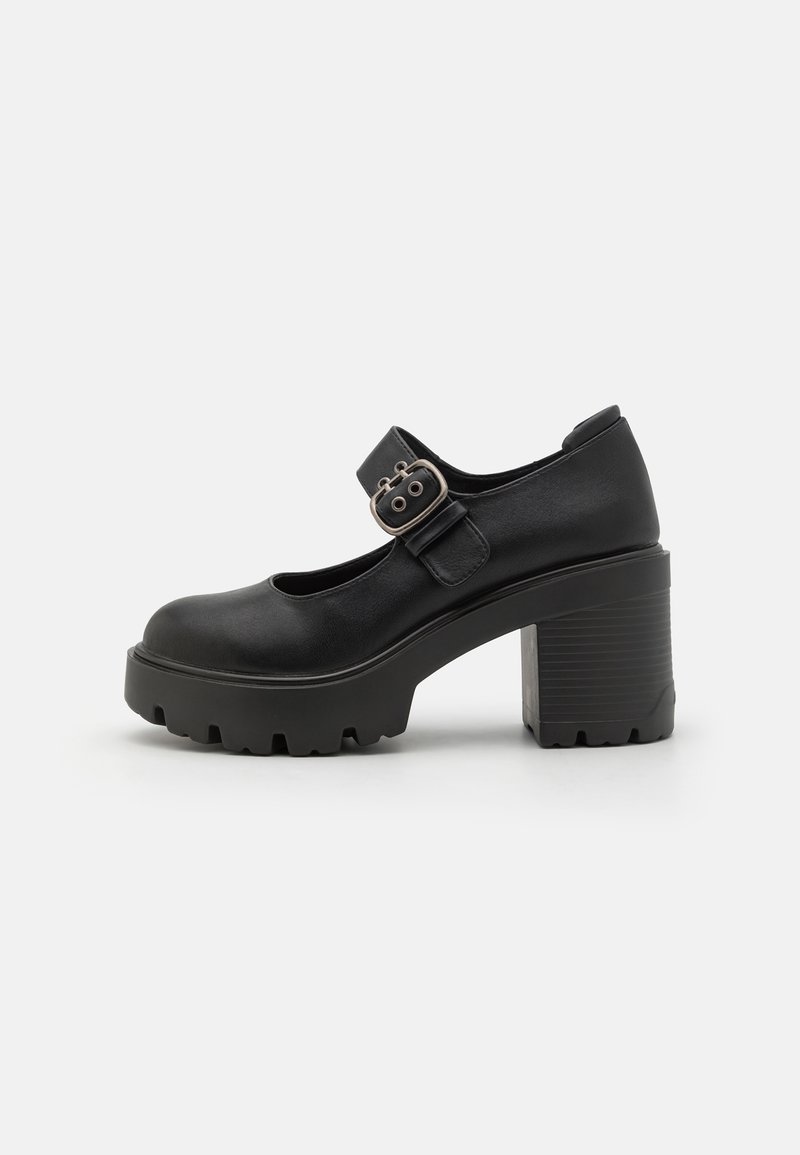 Chaussure Mary Jane noire avec talon bloc épais, semelle à crampons et bride boucle argentée sur le cou-de-pied, présentée sur fond blanc.