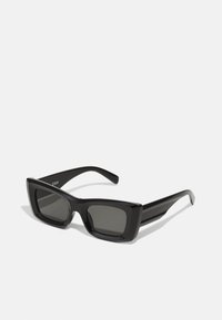 Lunettes de soleil noires carrées avec monture en plastique épaisse, verres sombres et design épuré. Présente un branding minimal sur les branches. Vue de face.
