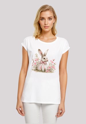 Weißes T-Shirt mit kurzen Ärmeln, das eine Illustration eines grauen Kaninchens mit einer rosa Schleife zeigt, umgeben von rosa Blumenakzenten. Aus glattem Baumwollstoff.