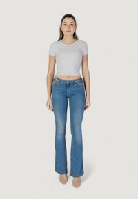 Top corto a coste grigio chiaro con orli a scallop, abbinato a jeans blu svasati con cuciture decorative sulla vita. Scarpe beige.