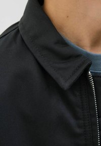 Närbild av en person som bär en svart jacka med dragkedja och en blå T-shirt med rund hals under.