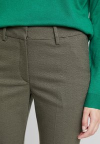 Olivově zelené kalhoty na míru s texturovaným povrchem, slim fit, s poutky na opasek a hladkým předním designem, spárované se zeleným svetrem.