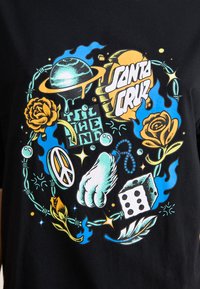 Black cotton T-shirt featuring a colorful graphic with a planet, roses, a peace sign, dice, and text. Design includes green and blue accents.