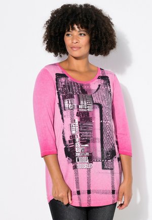 Haut rose à manches trois quarts avec texte graphique noir et motifs, arborant un col rond et un ourlet légèrement incurvé.