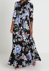 Robe maxi fleurie avec un fond noir, des manches longues et un col boutonné. Décorée de fleurs colorées et d'une silhouette fluide.