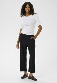 Witte, korte mouwen, getailleerde top gecombineerd met zwarte, wijde broek. De broek heeft zijzakken. Draag het met donkerrode schoenen.