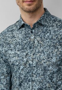 Chemise à manches longues à motifs floraux avec une base bleu foncé, ornée d'accents bleu clair et beige ; confectionnée dans un tissu texturé ; col pointu.