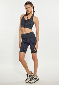 Sötét szürke camo mintás sport melltartó és kerékpáros short szett. A felső rész cipzárral záródik, a sima, rugalmas anyag kényelmet biztosít.