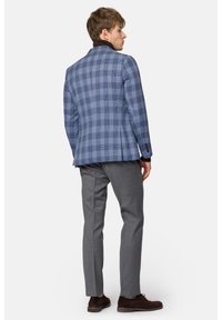 Niebiesko-szary marynarka w kratę o dopasowanym kroju, brązowy kołnierz oraz szare spodnie. Wyjątkowe detale to zapinane mankiety i subtelna faktura.