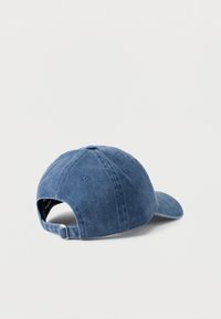 Gorra de mezclilla azul con visera curva, correa ajustable en la parte trasera y costuras visibles. Presenta una textura suave y seis orificios de ventilación.