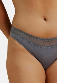 Le string en dentelle grise est confectionné dans un tissu doux, avec un bord festonné le long de la taille et une silhouette ajustée.