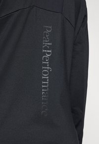 Black athletic jacket with textured fabric, featuring a vertical embossed logo "PeakPerformance" on the back. Design includes a subtle seam detailing.