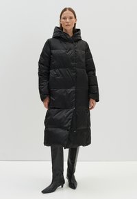 Zwarte puffer jas met een capuchon, lange mouwen, knoopsluiting en een gewatteerd ontwerp. Gemaakt van glanzend, lichtgewicht materiaal met een soepele textuur.