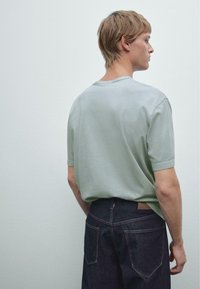 Mint green short-sleeve t-shirt made of soft fabric, with a relaxed fit and crew neckline, paired with dark denim jeans featuring back pockets.